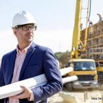 Confident architect holding rolled up blueprints at construction site - Architecture GOLN [ en.architecture.gurukul.edu.bd ]